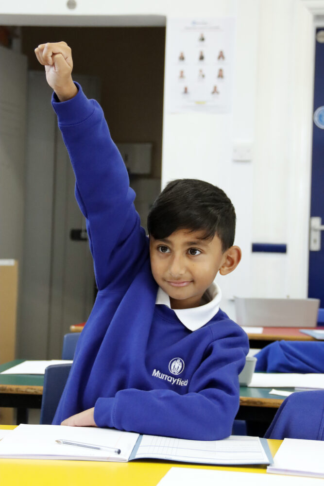 An eager pupil holds his hand high in the air ready to be picked to answer the question posed by the teacher