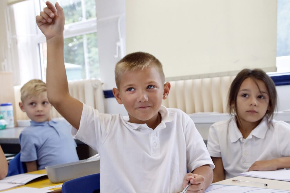 A young pupil raises his hand to answer