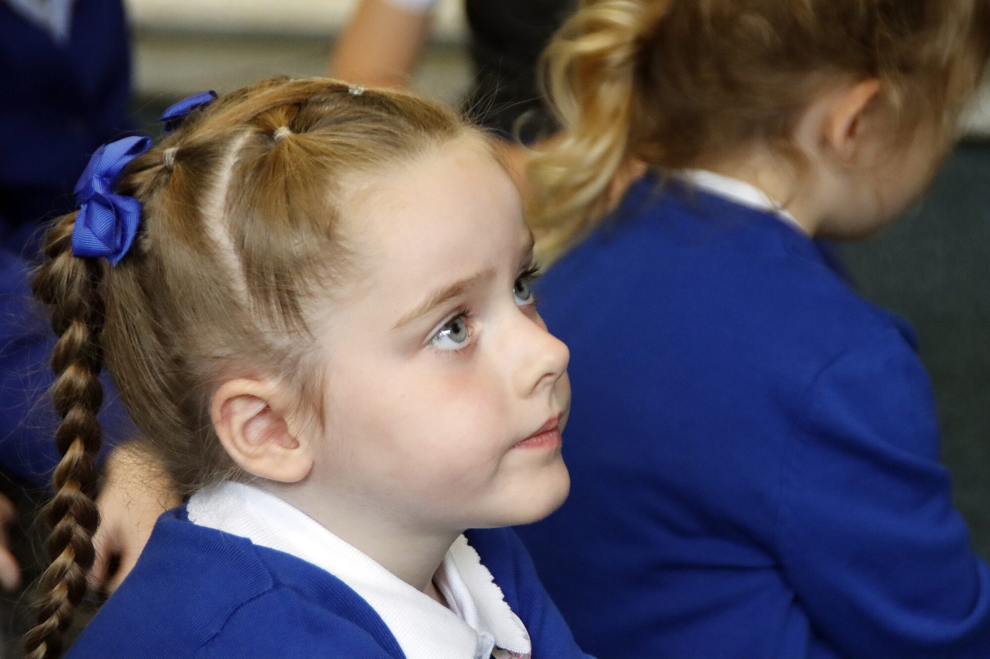 A young girl pupil with blue ribbons in her hair gazes upward paying attention to the lesson