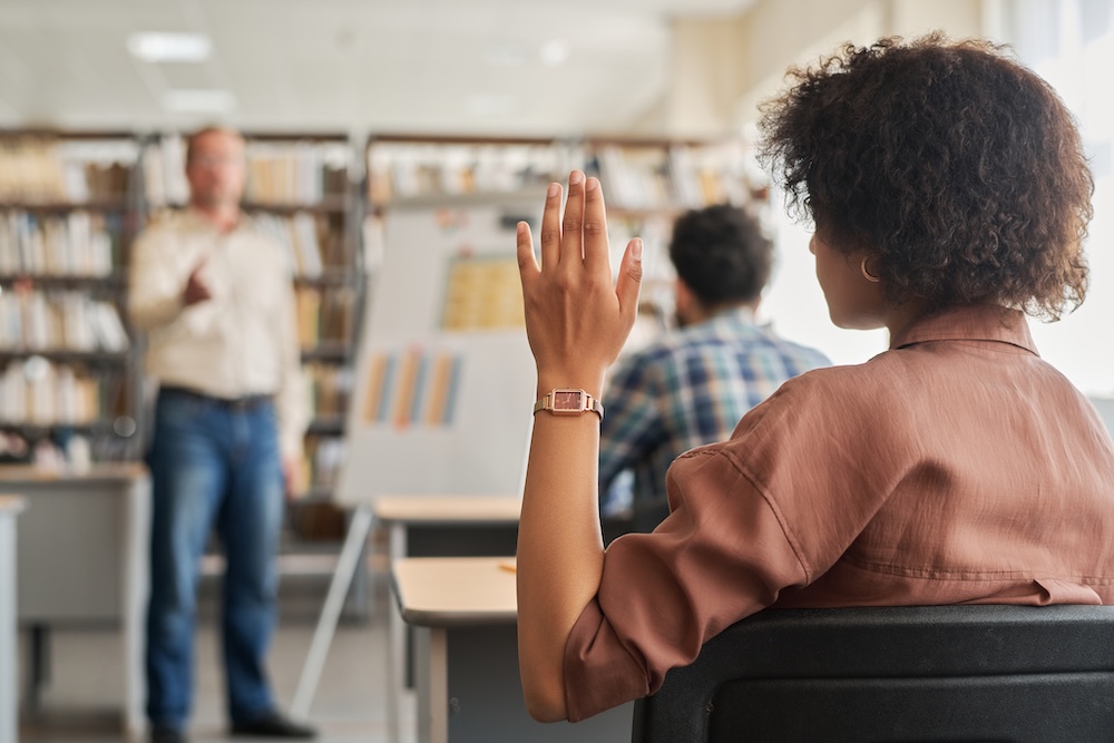 Rear view of woman raising her arm up and answering in class